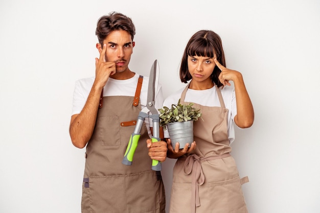 Young mixed race gardener couple isolated on white background pointing temple with finger, thinking, focused on a task.