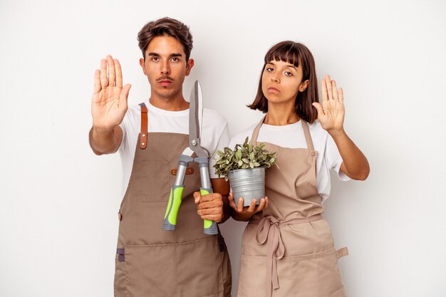 Young mixed race gardener couple isolated on white background standing with outstretched hand showing stop sign, preventing you.