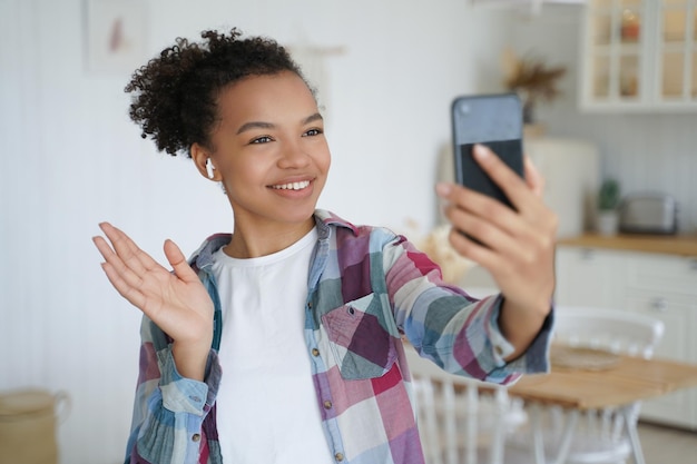 Young mixed race girl blogger holds smartphone use video call greeting followers in social network