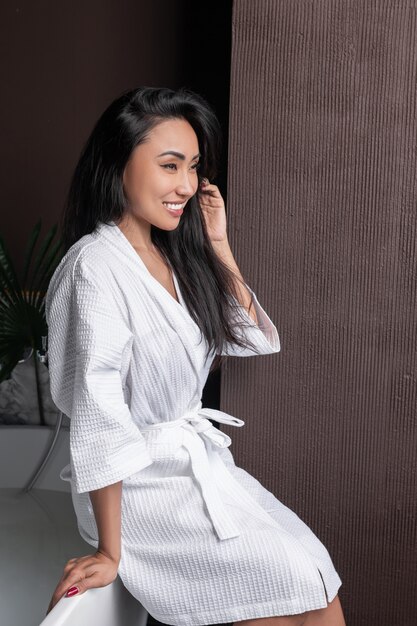 Young mixed-race girl posing sitting in a white bathrobe near a bathtub with typed water