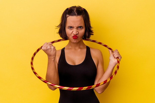 Young mixed race gymnastic woman isolated on yellow background showing fist to camera, aggressive facial expression.