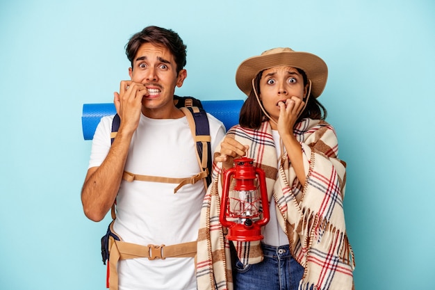 Young mixed race hiker couple isolated on blue background biting fingernails, nervous and very anxious.