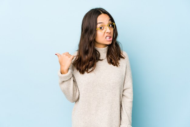 Young mixed race hispanic woman shocked pointing with index fingers to a copy space.