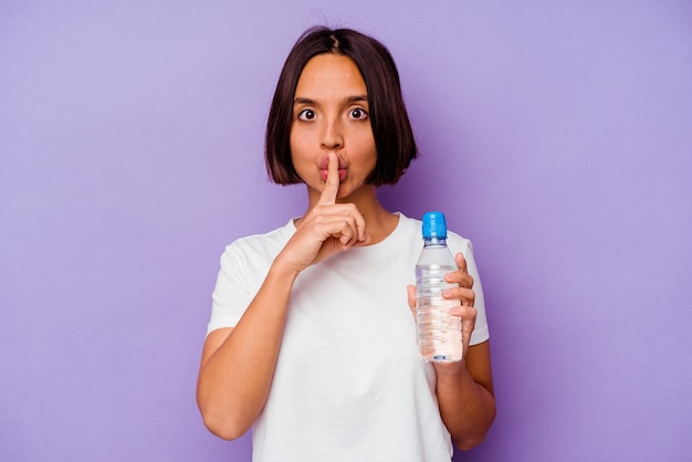 Young mixed race holding a water bottle isolated on purple background keeping a secret or asking for silence.