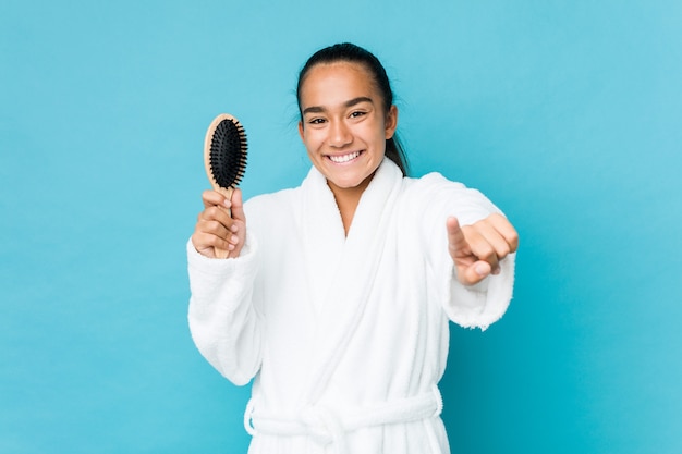 Young mixed race indian holding an hairbrush cheerful smiles pointing to front.