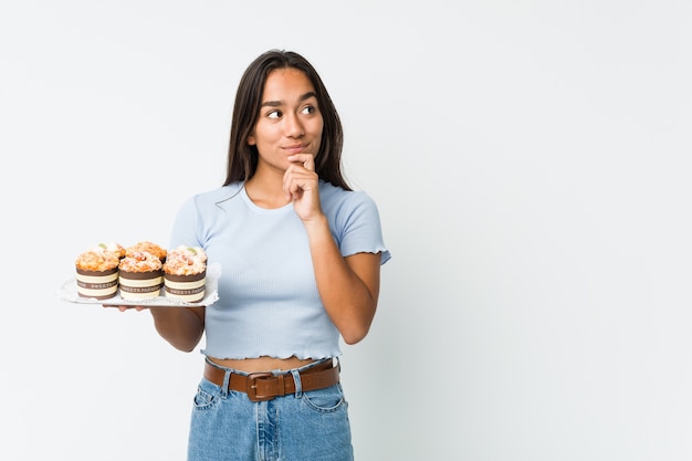 Young mixed race indian holding a sweet cakes looking sideways with doubtful and skeptical expression.