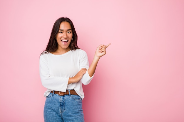 Young mixed race indian woman smiling cheerfully pointing with forefinger away.