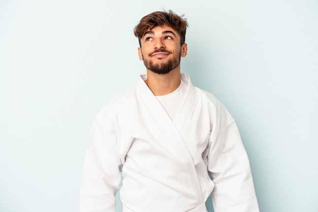 Young mixed race man doing karate isolated on blue background dreaming of achieving goals and purposes