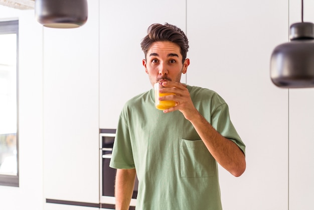 Young mixed race man drinking orange juice in his kitchen