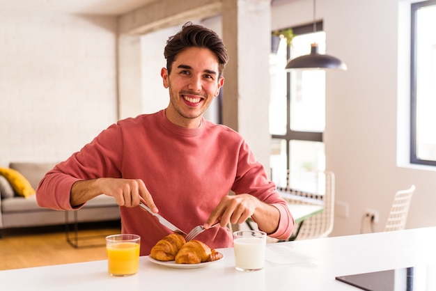 朝の台所でクロワッサンを食べる若い混血の男