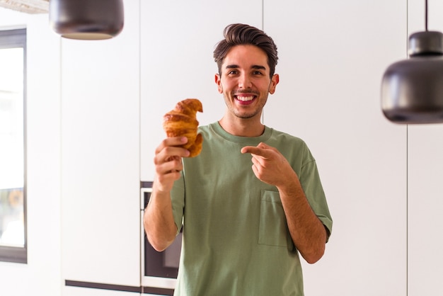 Young mixed race man eating croissant in a kitchen on the morning