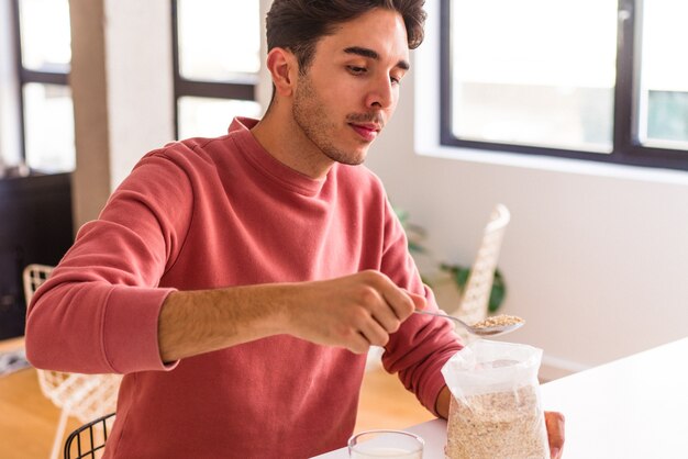 Young mixed race man eating oatmeal and milk for breakfast in his kitchen