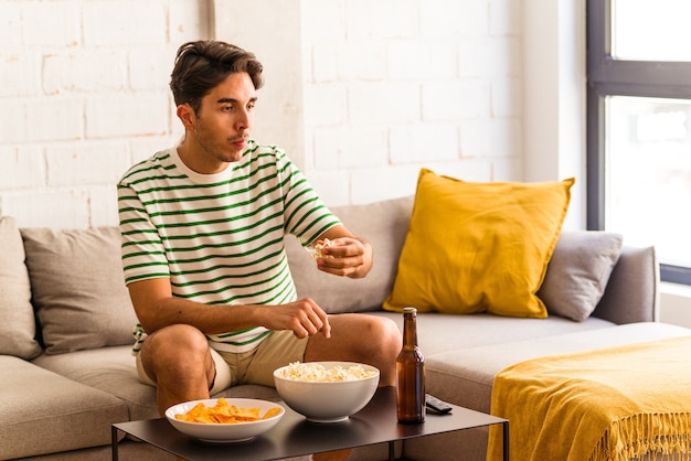 Young mixed race man eating popcorn sitting on the sofa