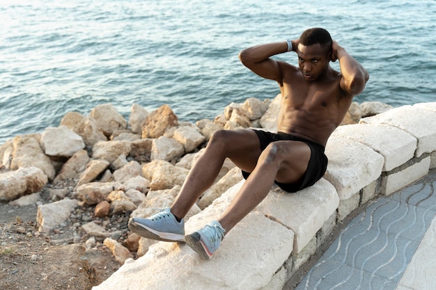 Young mixed race man exercising on the beach and doing sit ups with concentrated face