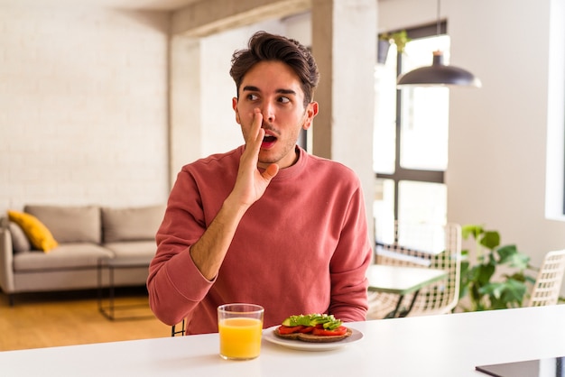 Young mixed race man having breakfast in his kitchen is saying a secret hot braking news and looking aside