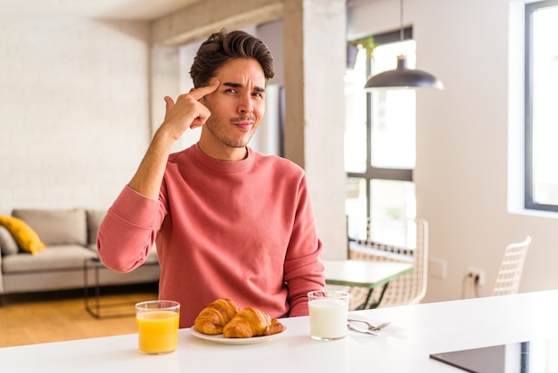 Young mixed race man having breakfast in a kitchen on the morning pointing temple with finger, thinking, focused on a task.