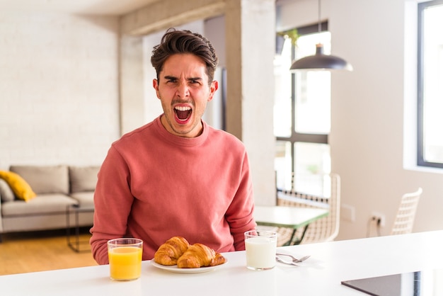 非常に怒って攻撃的な叫び声で朝にキッチンで朝食をとっている若い混血の男。