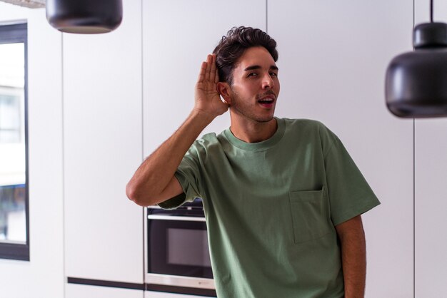 Young mixed race man in his kitchen trying to listening a gossip.