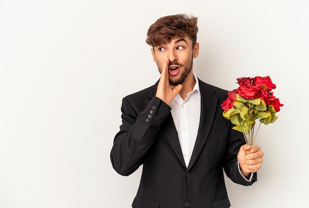 Young mixed race man holding bouquet of roses isolated on white background is saying a secret hot braking news and looking aside