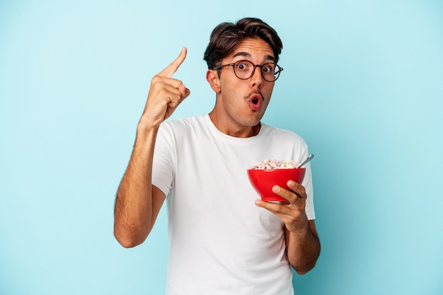 Young mixed race man holding cereals isolated on blue background having an idea, inspiration concept.