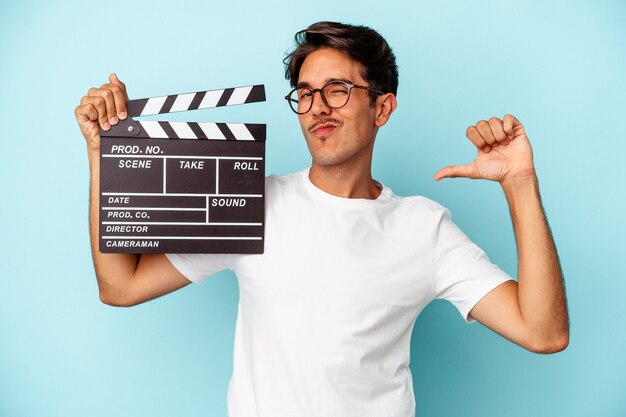 Young mixed race man holding clapperboard isolated on blue background feels proud and self confident, example to follow.