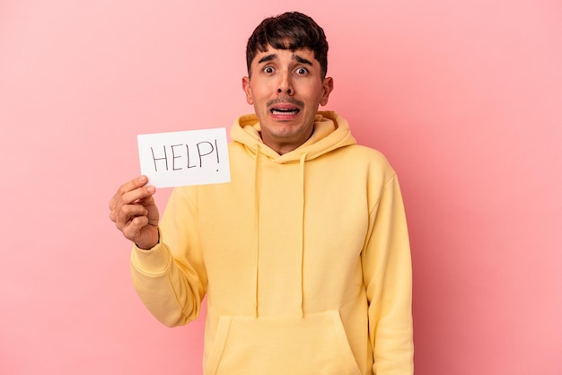 Young mixed race man holding a help placard isolated on pink background