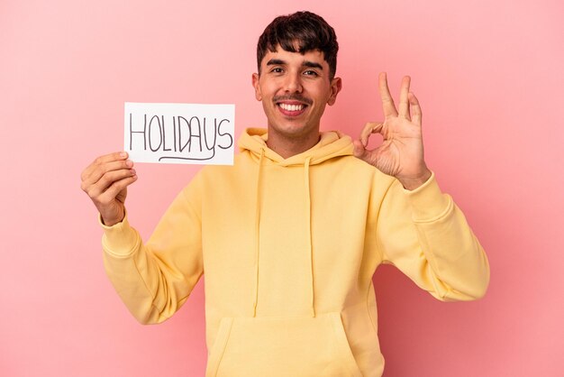 Young mixed race man holding a holidays placard isolated on pink background