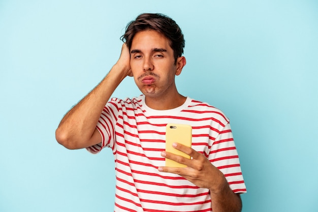 Young mixed race man holding mobile phone isolated on blue background being shocked, she has remembered important meeting.