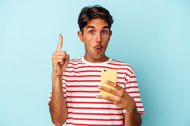 Young mixed race man holding mobile phone isolated on blue background having some great idea, concept of creativity.