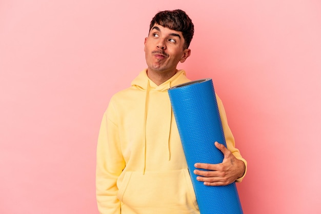 Young mixed race man holding a sport mat isolated on pink background dreaming of achieving goals and purposes