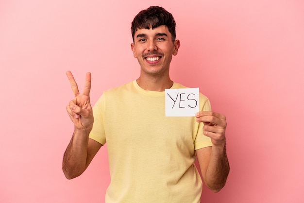 Young mixed race man holding yes placard isolated on pink background