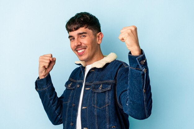 Young mixed race man isolated on blue background cheering carefree and excited. Victory concept.