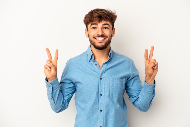 Young mixed race man isolated on grey background showing victory sign and smiling broadly.