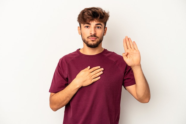 Young mixed race man isolated on grey background taking an oath, putting hand on chest.