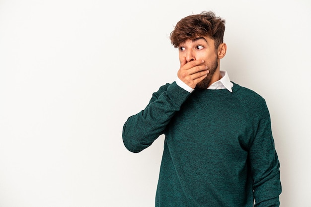 Young mixed race man isolated on grey background thoughtful looking to a copy space covering mouth with hand.