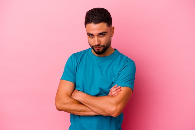 Young mixed race man isolated on pink background frowning face in displeasure, keeps arms folded.