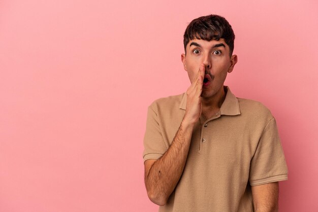 Young mixed race man isolated on pink background is saying a secret hot braking news and looking aside