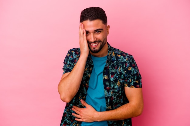 Young mixed race man isolated on pink background laughs happily and has fun keeping hands on stomach.