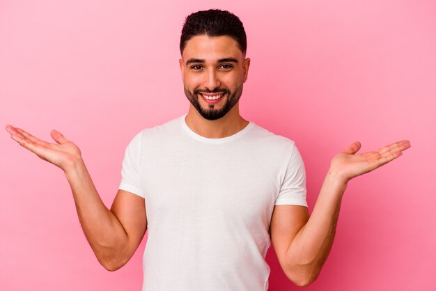 Young mixed race man isolated on pink background makes scale with arms, feels happy and confident.