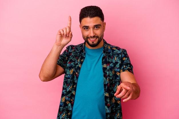 Young mixed race man isolated on pink background pointing to different copy spaces, choosing one of them, showing with finger.