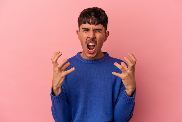 Young mixed race man isolated on pink background screaming with rage.