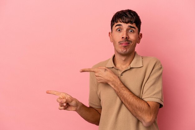 Foto giovane uomo di razza mista isolato su sfondo rosa scioccato che punta con il dito indice a uno spazio di copia.