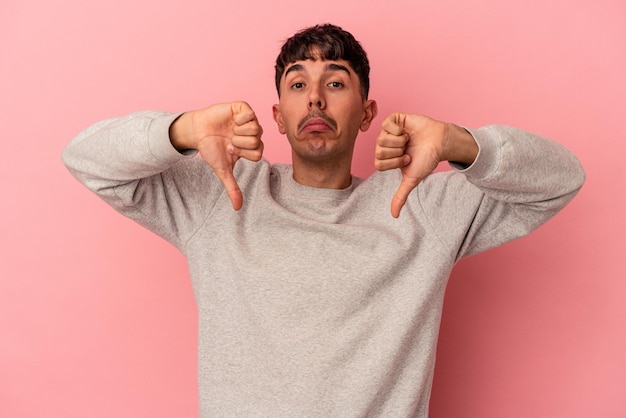 Young mixed race man isolated on pink background showing a dislike gesture, thumbs down. Disagreement concept.