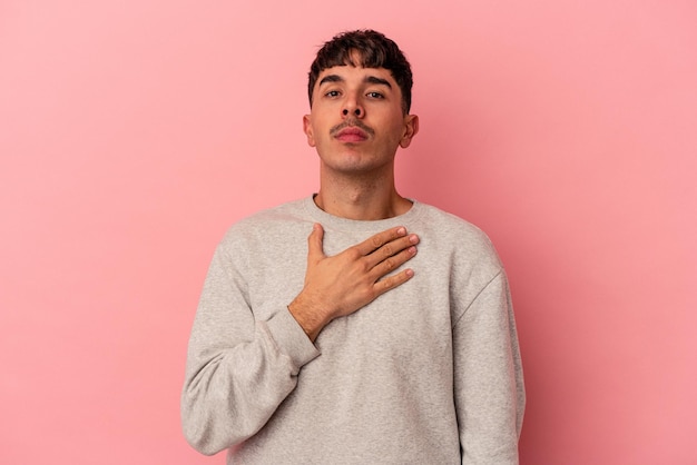 Young mixed race man isolated on pink background taking an oath putting hand on chest