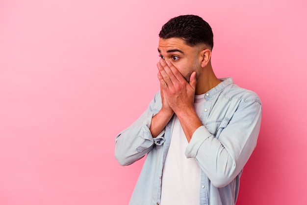 Young mixed race man isolated on pink background thoughtful looking to a copy space covering mouth with hand.