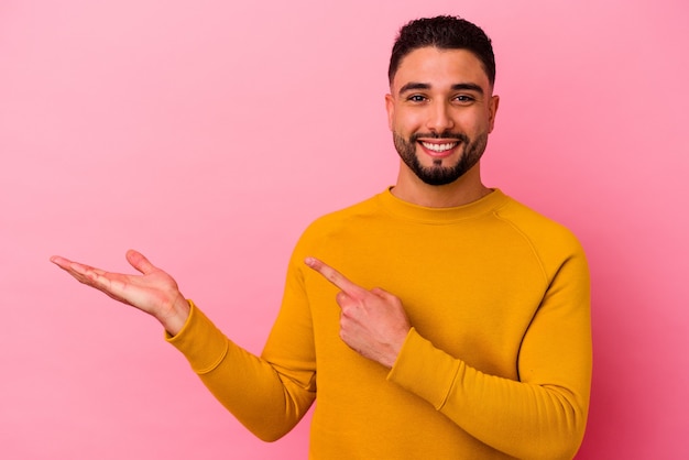 Young mixed race man isolated on pink excited holding a copy space on palm.