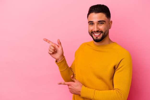 Young mixed race man isolated on pink pointing with forefingers to a copy space, expressing excitement and desire.