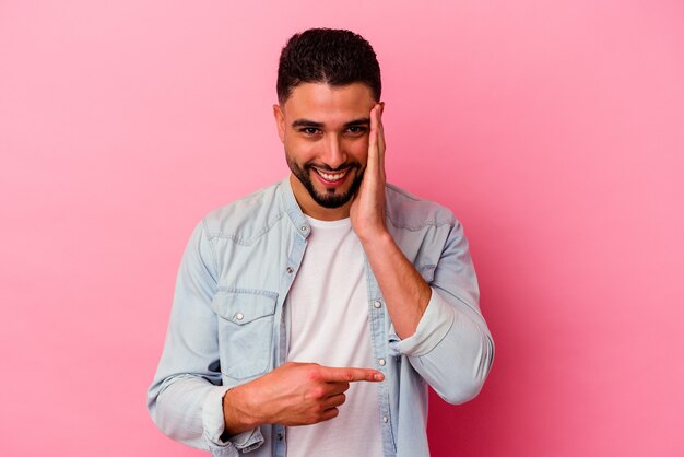 Young mixed race man isolated on pink saying a gossip, pointing to side reporting something.