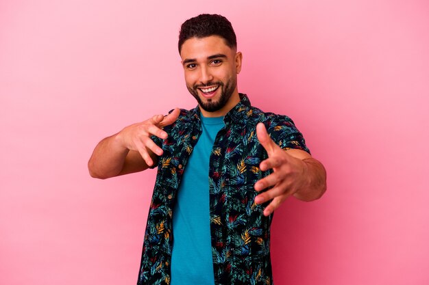 Young mixed race man isolated on pink wall feels confident giving a hug to the camera.