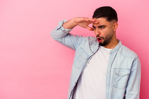 Young mixed race man isolated on pink wall looking far away keeping hand on forehead.